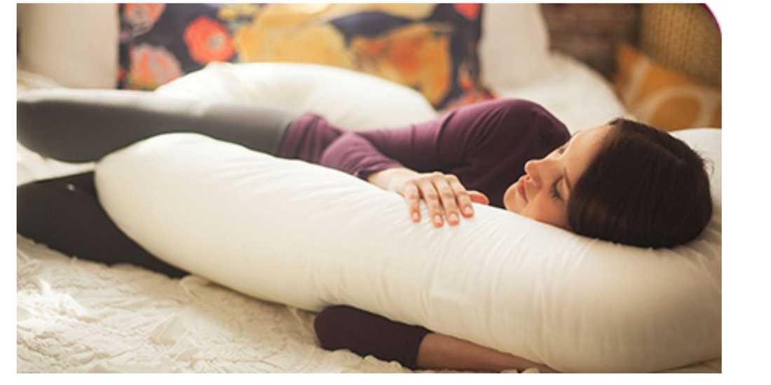 Image of a pregnant woman lying on her side with two C-shaped pillows, one supporting her head and the other wrapped around her back and between her legs for support.