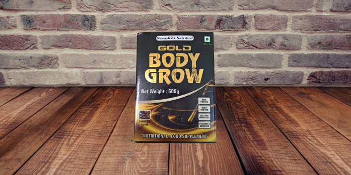 mage of a container of Body Grow Gold Body Gain Powder, a protein supplement for muscle building and development, with a scoop of powder resting on top of it.